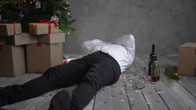 a drunken, bearded bald man wakes up in the morning after a corporate party on Christmas or New Year's, picks up a bottle of wine under the tree and gets hungover.