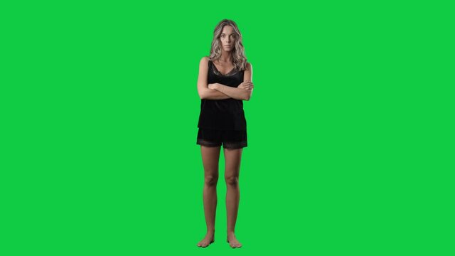 Standing young woman in black silk sleepwear crossing hands looking at camera. Full body isolated on green screen background