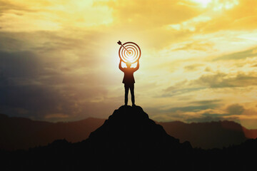 Silhouette of businessman holding a target board on top of mountain. Concept of aim and objective...