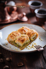Turkish or Bosnian dessert called Baklava with pistachio served with traditional Turkish or Bosnian coffee set on a wooden board in moody atmosphere
