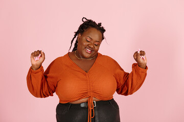 Excited young black plus size body positive woman with dreadlocks in orange top happy of big win poses for camera on pink background in studio closeup