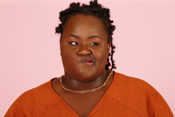 Skeptical young black plus size body positive woman makes a grimace and squints on pink background in studio closeup