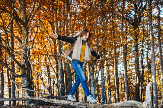 Smiling woman with arms outstretched balancing on tree trunk