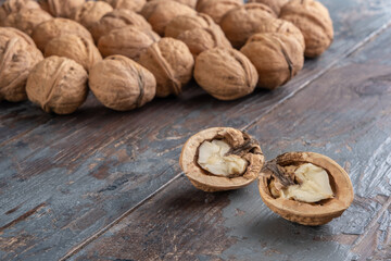 Two pretty halves of a ripe split walnut with a light, tasty core, a scattering of whole in-shell walnuts vaguely visible in the distance, against a textured vintage wooden background.
