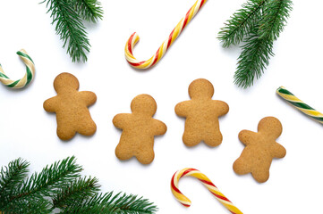 Christmas gingerbread cookies in the shape of man with lollipops and fir branches on white background, top view