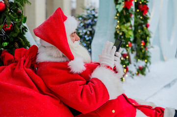 Santa claus using the phone outdoors. Merry Christmas.