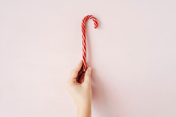 Christmas candy cane in hand on pink background.