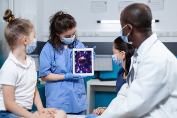 Pediatrician woman nurse with protective face mask against coronavirus holding tablet computer with virus expertise on screen. Medical team discussing covid19 symptoms. Health care service