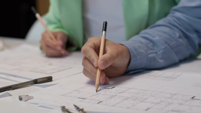 Architect or designer works on house layout close up. Creative person at table writing on blueprint or draft design of modern building manufacture. Adult specialist making prototype of home planning