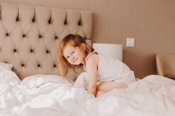 Cute toddler girl having fun in bed with white linen.