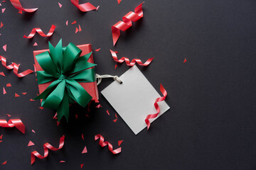 close up top view of christmas gift box with red rolling ribbon and confetti on black background with copy space for black Friday shopping season and happy new year festival concept