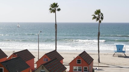 Colorful waterfront cottages, Oceanside California USA. Multicolor bungalow huts, summer sea, beachfront lodging. Many vacation houses on beach, ocean waves and palm trees. Lifeguard tower, watchtower