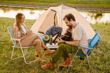 White couple playing guitar while resting during camping together