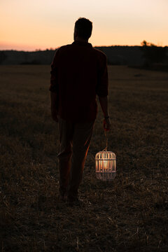 Man standing on grass holding illuminated bird cage