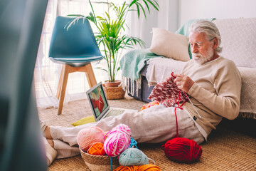 Senior man learning to knit wool through laptop at home