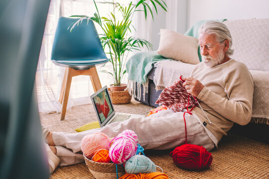 Senior man learning to knit wool through laptop at home