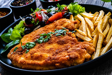 Breaded fried pork chop with French fries and fresh vegetables on wooden table
