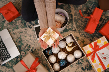 Christmas background with decorations and gift boxes. Woman hands holding wrapped white box with golden bow.