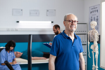 Obraz premium Portrait of elder patient at physiotherapy clinic for recovery. Senior man preparing for gymnastics to recover muscle injury with physical exercise. Person with orthopedic therapy