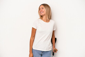 Fototapeta premium Young caucasian woman holding crutch isolated on white background looks aside smiling, cheerful and pleasant.