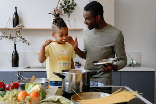 Young man talking with son smelling spaghetti in kitchen