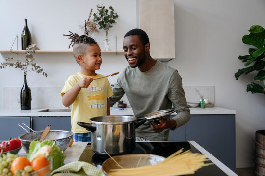 Smiling boy showing spaghetti to father in kitchen