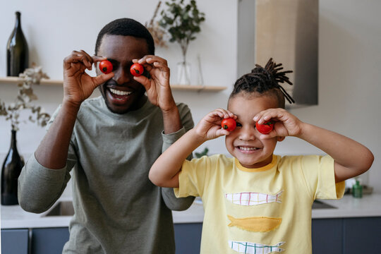 Cheerful father and son holding tomatoes in front of eyes at home