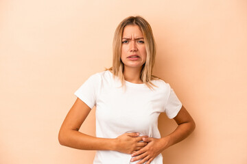 Young caucasian woman isolated on beige background having a liver pain, stomach ache.