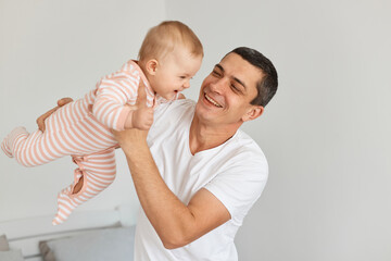 Happy excited attractive young adult father with his toddler baby girl playing together at home, playing with flying kid, expressing positive emotions.