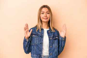 Young caucasian woman isolated on beige background holding something little with forefingers, smiling and confident.