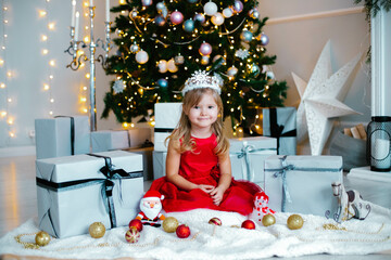 Christmas,x-mas,winter concept - girl in red dress celebrates the New Year near the christmass tree in a room