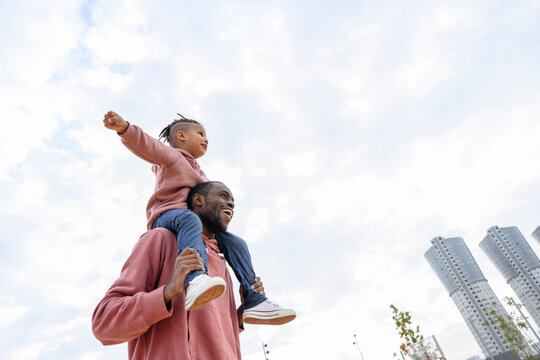 Playful boy sitting with arms outstretched on man's shoulders