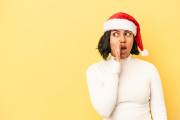 Young latin woman celebrating christmas isolated on yellow background is saying a secret hot braking news and looking aside