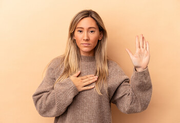 Young caucasian woman isolated on beige background taking an oath, putting hand on chest.
