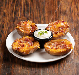 Aperitivo patatas al horno con jamón y queso con salsa de yogurt sobre tabla de madera