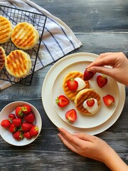 The girl's hand decorates freshly prepared cheesecakes with fresh red strawberries
