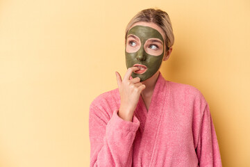 Young caucasian woman wearing face mask isolated on yellow background relaxed thinking about something looking at a copy space.