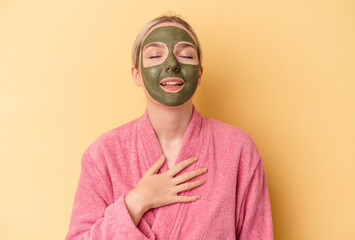 Young caucasian woman wearing face mask isolated on yellow background laughs out loudly keeping hand on chest.