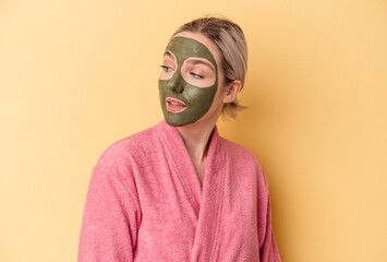 Young caucasian woman wearing face mask isolated on yellow background looks aside smiling, cheerful and pleasant.