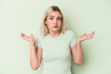 Young caucasian woman isolated on green background doubting and shrugging shoulders in questioning gesture.