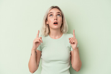 Young caucasian woman isolated on green background pointing upside with opened mouth.