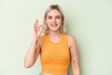 Young caucasian woman isolated on green background cheerful and confident showing ok gesture.