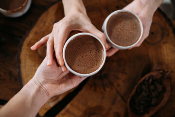 Hot handmade ceremonial cacao in white cups. Woman hands giving craft cocoa, top view on wooden...