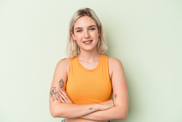 Young caucasian woman isolated on green background who feels confident, crossing arms with determination.