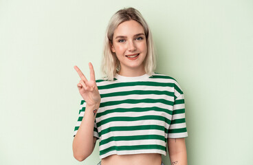 Young caucasian woman isolated on green background showing victory sign and smiling broadly.