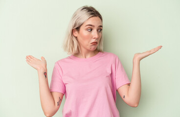 Young caucasian woman isolated on green background confused and doubtful shrugging shoulders to...