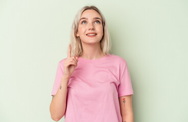 Young caucasian woman isolated on green background indicates with both fore fingers up showing a...