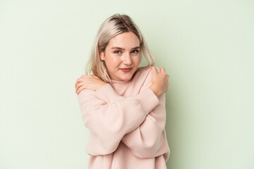 Young caucasian woman isolated on green background hugs, smiling carefree and happy.