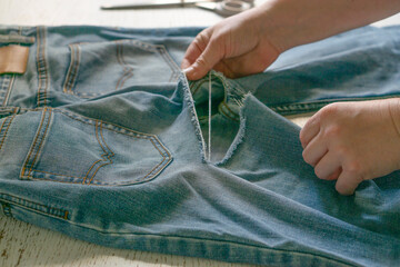 Female hands with old torn jeans spread out on the table. The concept of clothing repair,...