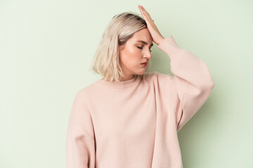 Young caucasian woman isolated on green background forgetting something, slapping forehead with palm and closing eyes.